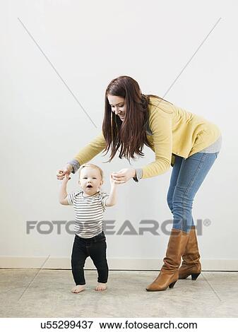 Stock Photo - Baby girl (12-17 months) walking while mother assisting her. Fotosearch