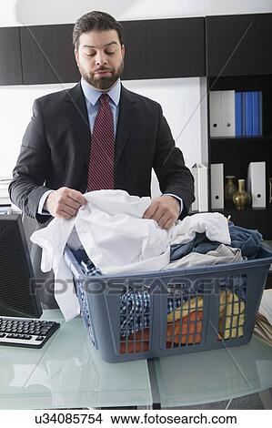 Picture - Businessman looking through laundry basket in office. Fotosearch