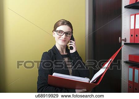 Stock Photo - Businesswoman reading files and talking on cell phone. Fotosearch