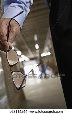 Close up of man holding eyeglasses in warehouse View Large Photo Image Picture - Close up of man holding eyeglasses in warehouse. Fotosearch