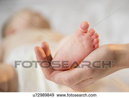 Close up of mother's hand holding tiny foot of baby girl (6-11 months) View Large Photo Image Stock Photo - Close up of mother's hand holding tiny foot of baby girl (6-11 months). Fotosearch