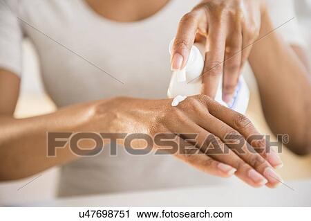 Stock Image - Close up of woman's hands applying moisturizer. Fotosearch