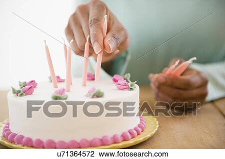 Stock Image - Close up of woman's hands putting candles on birthday cake. Fotosearch