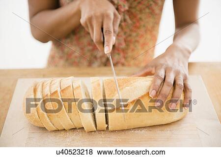 Stock Photo - Close up of womaqn's hand cutting bread. Fotosearch