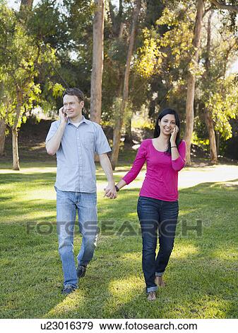 Stock Photo - Couple walking and using mobile phone in park. Fotosearch