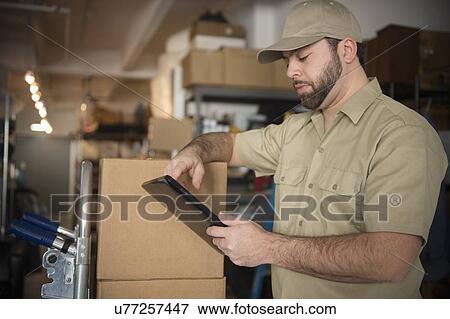 Delivery man in warehouse holding portable information device View Large Photo Image Stock Photo - Delivery man in warehouse holding portable information device. Fotosearch