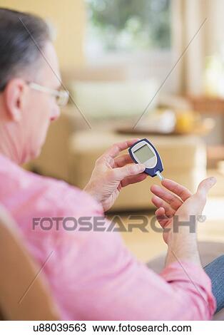 Stock Image - Diabetic man using glucose blood meter. Fotosearch