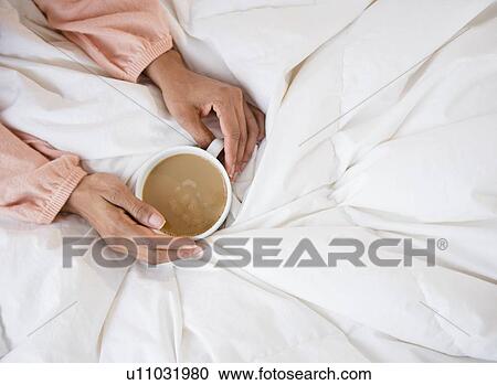 Stock Image - Elevated view of woman's hands holding coffee mug. Fotosearch