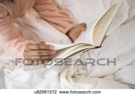 Stock Image - Elevated view of woman's hands holding book. Fotosearch