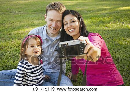Stock Photo - Family with daughter (4-5) playing in park and photographing themselves. Fotosearch