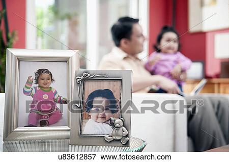 Stock Photo - Father and kid (6-11 months) and portraits in frames in foreground. Fotosearch