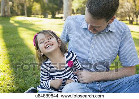 Picture - Father tickling his daughter (4-5 years) on sunny day in park. Fotosearch