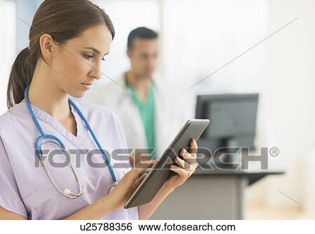 Stock Photograph - Female and male nurses working at nurse's station in hospital. Fotosearch
