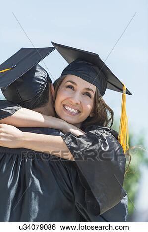 Stock Photograph - Female and male student embracing on graduation ceremony. Fotosearch