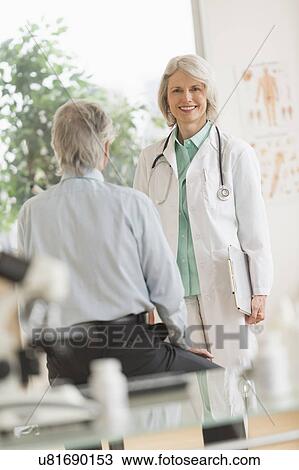 Stock Image - Female doctor talking to male patient in her office. Fotosearch
