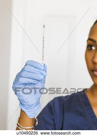 Stock Photography - Female nurse looking at thermometer. Fotosearch