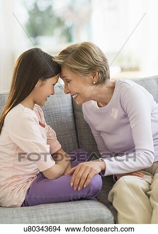 Granddaughter (8-9) and grandmother sitting on sofa and touching with heads View Large Photo Image Picture - Granddaughter (8-9) and grandmother sitting on sofa and touching with heads. Fotosearch