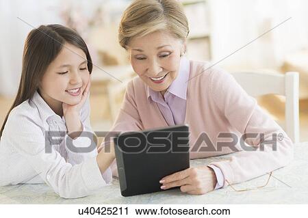 Stock Image - Granddaughter (8-9) and grandmother using digital tablet. Fotosearch