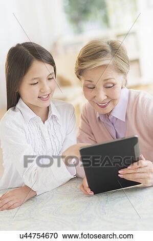 Stock Image - Granddaughter (8-9) and grandmother using digital tablet. Fotosearch