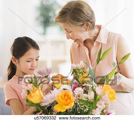 Stock Image - Granddaughter (8-9) and grandmother arranging flowers at home. Fotosearch