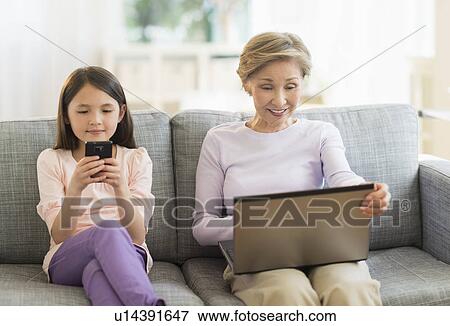 Granddaughter (8-9) and grandmother sitting on sofa and using laptop and cell phone View Large Photo Image Stock Photo - Granddaughter (8-9) and grandmother sitting on sofa and using laptop and cell phone. Fotosearch