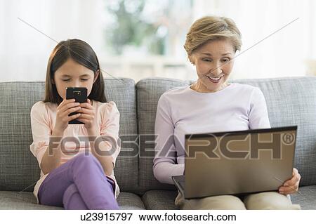 Granddaughter (8-9) and grandmother sitting on sofa and using laptop and cell phone View Large Photo Image Stock Photo - Granddaughter (8-9) and grandmother sitting on sofa and using laptop and cell phone. Fotosearch