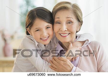 Stock Image - Granddaughter (8-9) embracing grandmother. Fotosearch