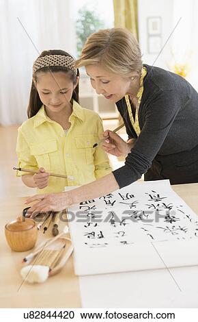 Stock Image - Grandmother and granddaughter (8-9) painting japanese symbols. Fotosearch