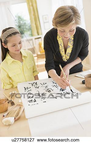 Stock Photo - Grandmother and granddaughter (8-9) painting japanese symbols. Fotosearch