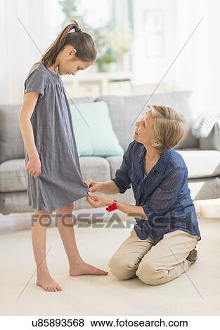 Stock Photo - Grandmother attaching sewing pins to granddaughter's (8-9) dress. Fotosearch