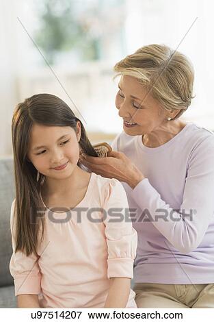 Stock Photo - Grandmother brushing granddaughter's (8-9) hair. Fotosearch