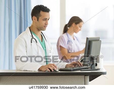 Stock Image - Male and female nurses working at nurse's station in hospital. Fotosearch
