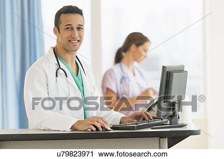 Stock Image - Male and female nurses working at nurse's station in hospital. Fotosearch