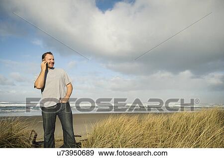 Man on phone while standing on beach View Large Photo Image Stock Photo - Man on phone while standing on beach. Fotosearch