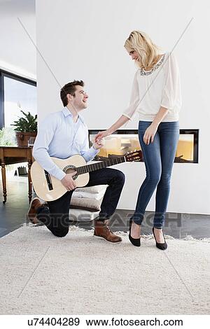 Stock Photo - Man playing guitar in front of woman. Fotosearch