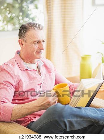 Stock Photo - Man sitting on sofa and reading book. Fotosearch