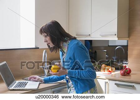 Mature woman using laptop while cooking View Large Photo Image Stock Photograph - Mature woman using laptop while cooking. Fotosearch