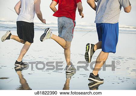 Stock Image - Men running on beach. Fotosearch