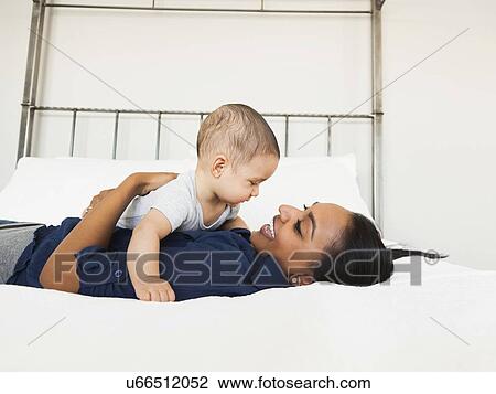 Stock Image - Mother holding her son (2-5 month), lying in bed happily. Fotosearch
