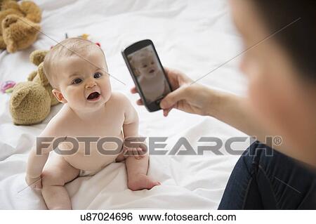 Mother photographing her baby daughter (6-11 months) with mobile phone View Large Photo Image Stock Photograph - Mother photographing her baby daughter (6-11 months) with mobile phone. Fotosearch