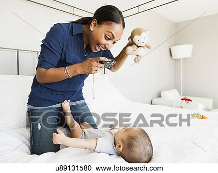 Stock Image - Mother playing with her son (2-5 months) taking his picture. Fotosearch