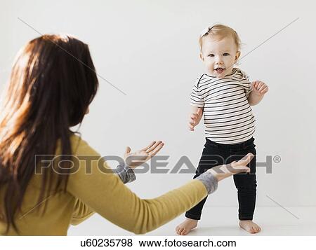 Stock Photo - Mother raising hands towards her daughter (12-17 months). Fotosearch