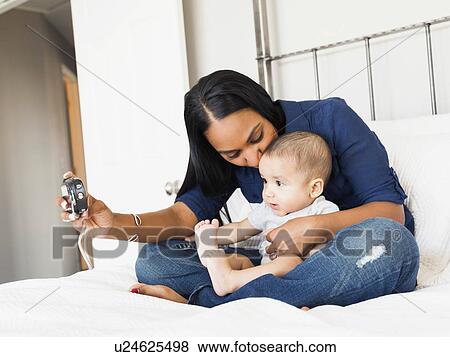 Stock Photo - Mother sitting n bed with her son (2-5 months) taking a picture. Fotosearch