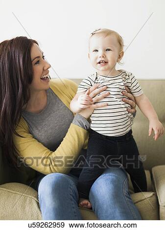 Mother with daughter (12-17 months) sitting on sofa View Large Photo Image Stock Photo - Mother with daughter (12-17 months) sitting on sofa. Fotosearch
