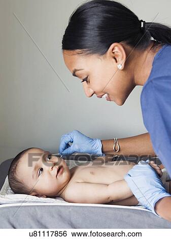 Stock Photograph - Nurse cleaning baby boy's (2-5 months) ear. Fotosearch