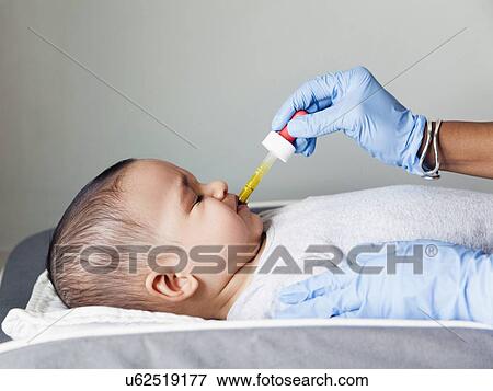 Stock Photo - Nurse giving baby boy's (2-5 months) medicine using pipette. Fotosearch