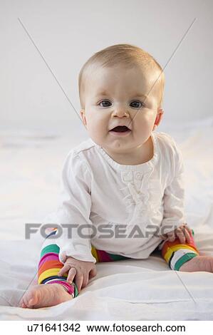 Stock Image - Portrait of baby girl (6-11 months) sitting in bed. Fotosearch