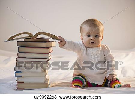 Stock Photo - Portrait of baby girl (6-11 months) sitting in bed with stack of books. Fotosearch