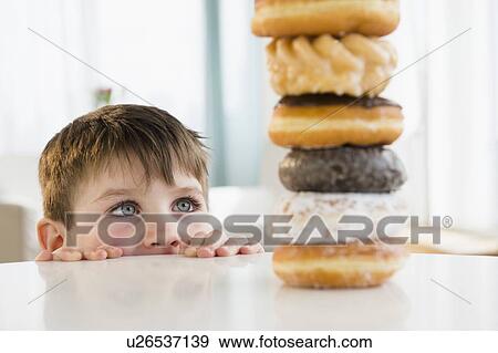 Stock Photo - Portrait of boy (4-5) looking at stacked donuts. Fotosearch