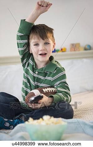 Stock Photo - Portrait of cheerful boy (4-5) sitting on bed, holding football. Fotosearch